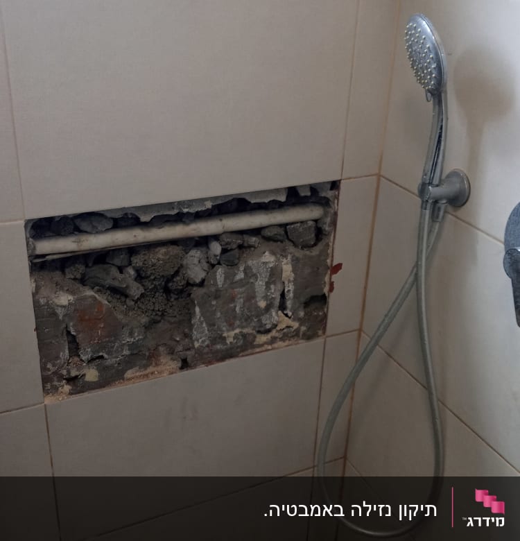 צינור חשוף בקיר מקלחת עם אריחים שבורים